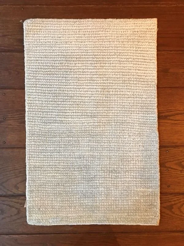 A rectangular cream-colored textured area rug on a wooden floor.
