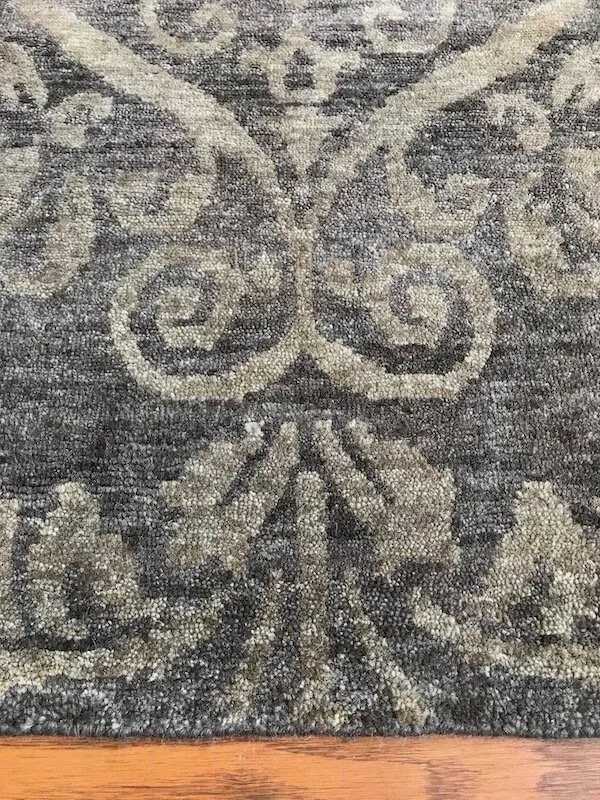 A close-up of a patterned rug with swirling floral and leaf motifs in shades of gray and beige.