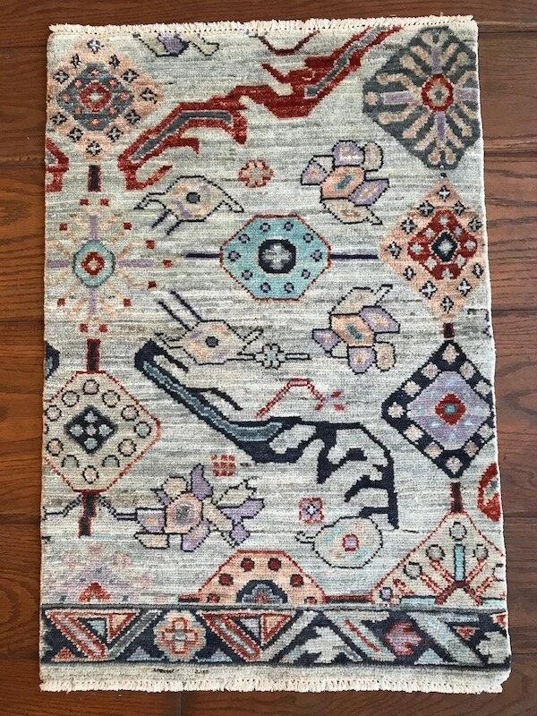 A patterned area rug with geometric shapes, floral motifs, and animal figures in shades of red, blue, purple, orange, and cream, placed on a wooden floor.