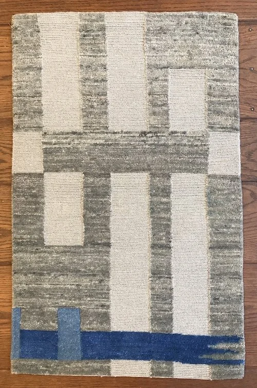 Abstract patterned rug with beige, gray, and blue geometric shapes on wooden floor.