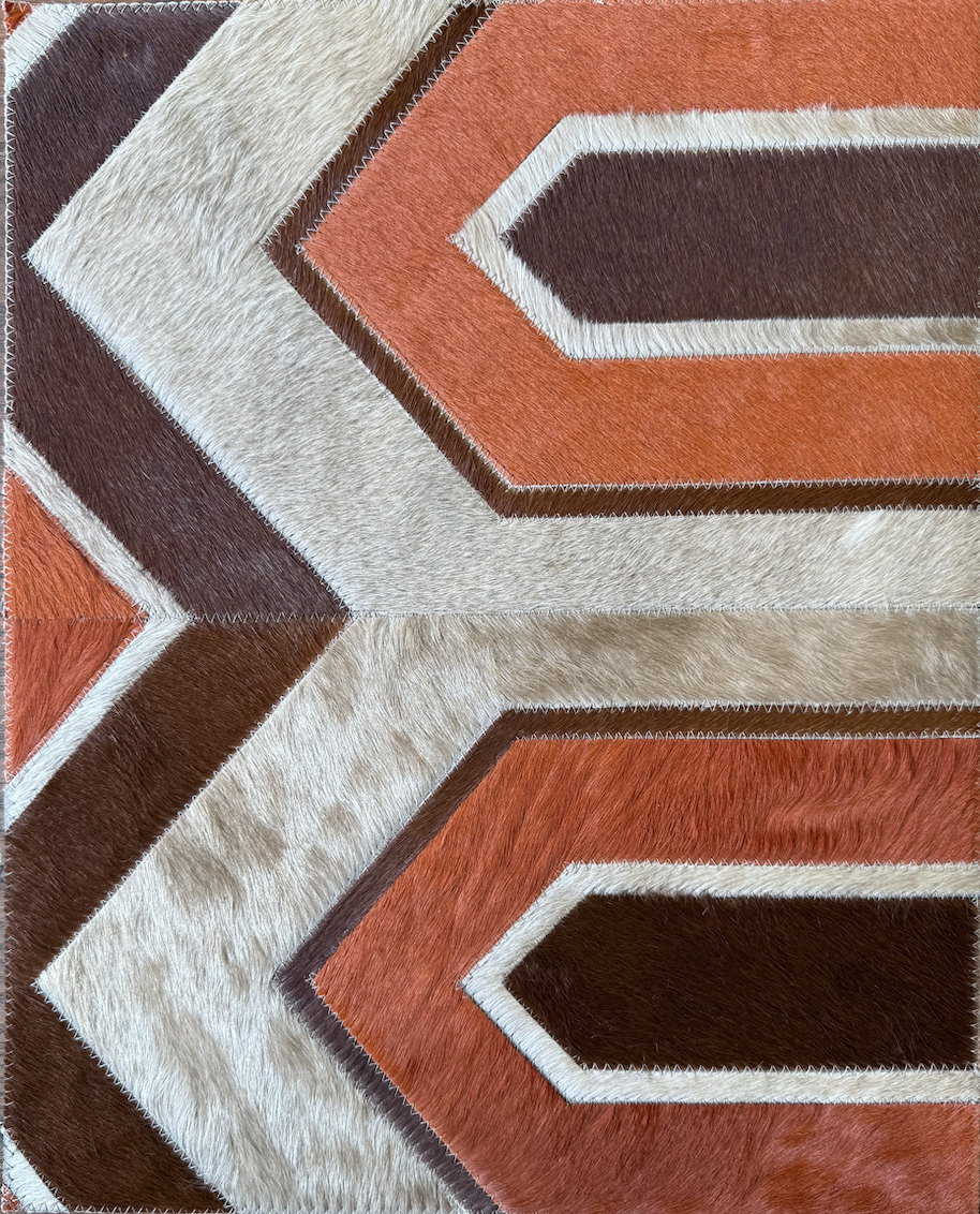 Close-up of a geometric area rug with zigzag and chevron patterns in shades of brown, cream, beige, and orange, featuring a textured, fur-like surface.
