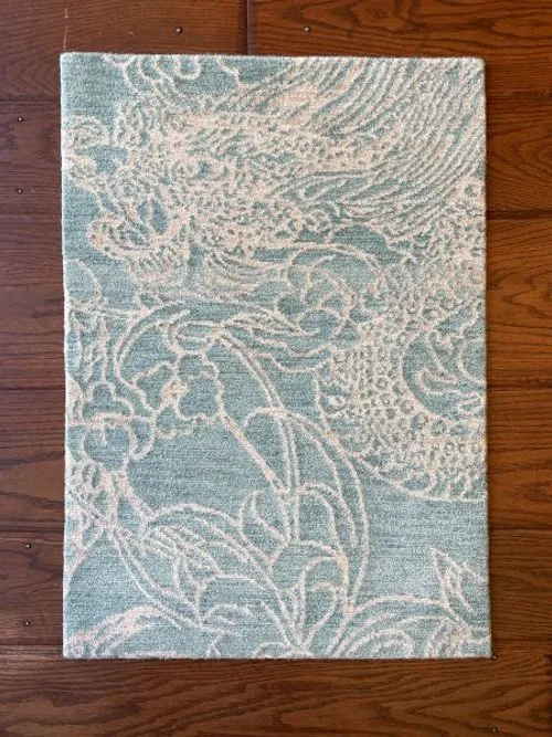 Light blue area rug with intricate cream-colored floral and vine pattern, placed on a wooden floor.