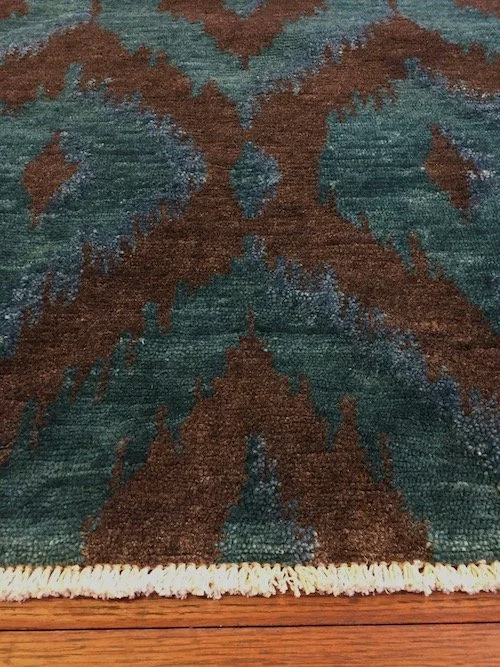 Close-up of a woven rug with a brown and teal geometric pattern on a wooden floor.