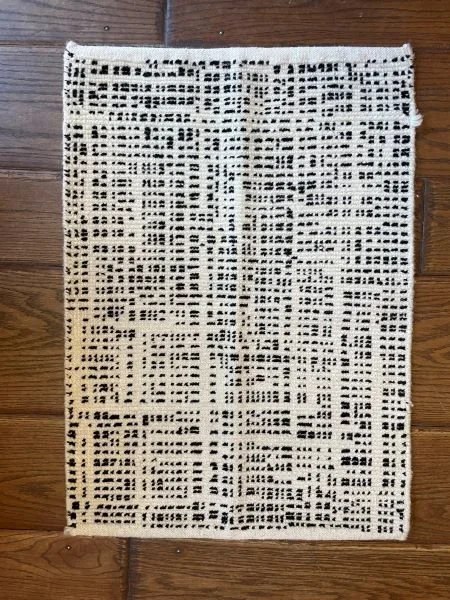 A rectangular area rug with a white background and black geometric and dotted patterns, placed on a wooden floor.