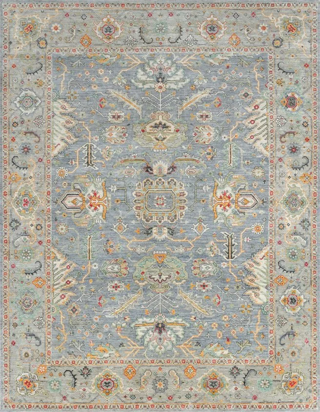 A traditional patterned area rug with a light blue background, intricate floral and geometric designs in shades of orange, cream, red, black, and gray, bordered by a detailed border with floral motifs.