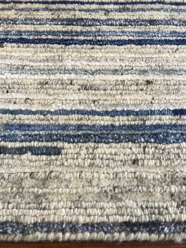 Close-up of a striped woven rug with shades of beige, gray, and blue.