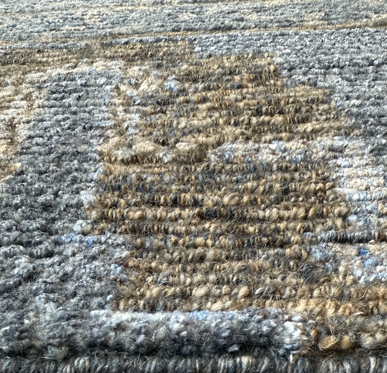 Close-up of a textured woven rug with shades of brown, gray, and black fibers.