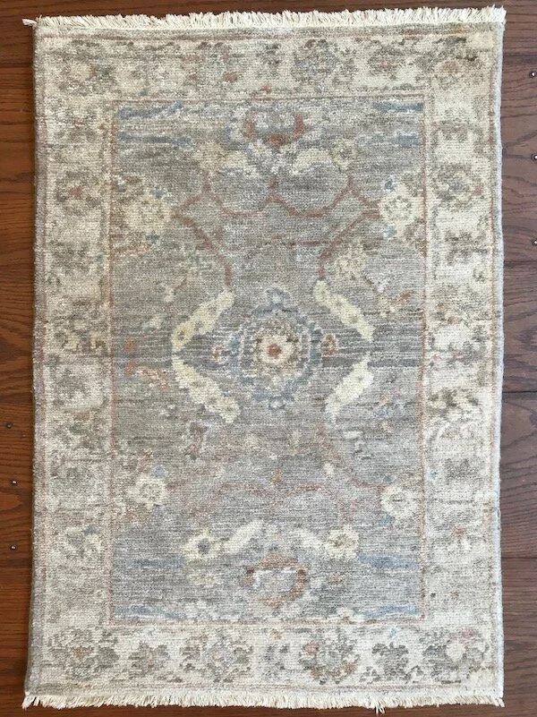 Vintage beige and light blue patterned area rug with floral motifs and a distressed appearance on a wooden floor.