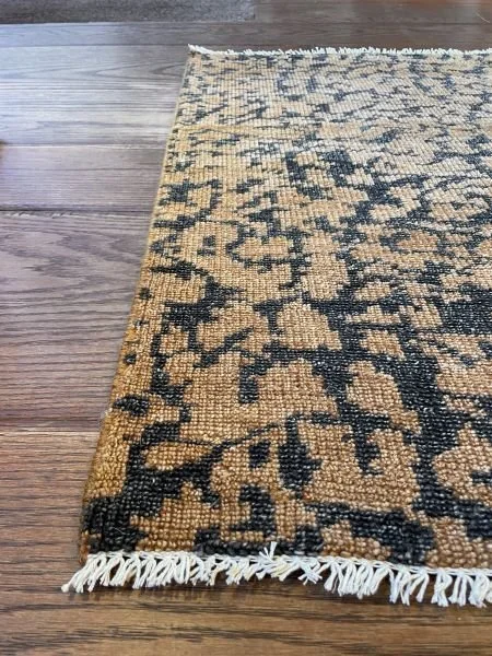 Close-up of a patterned rug with fringe on a wooden floor.