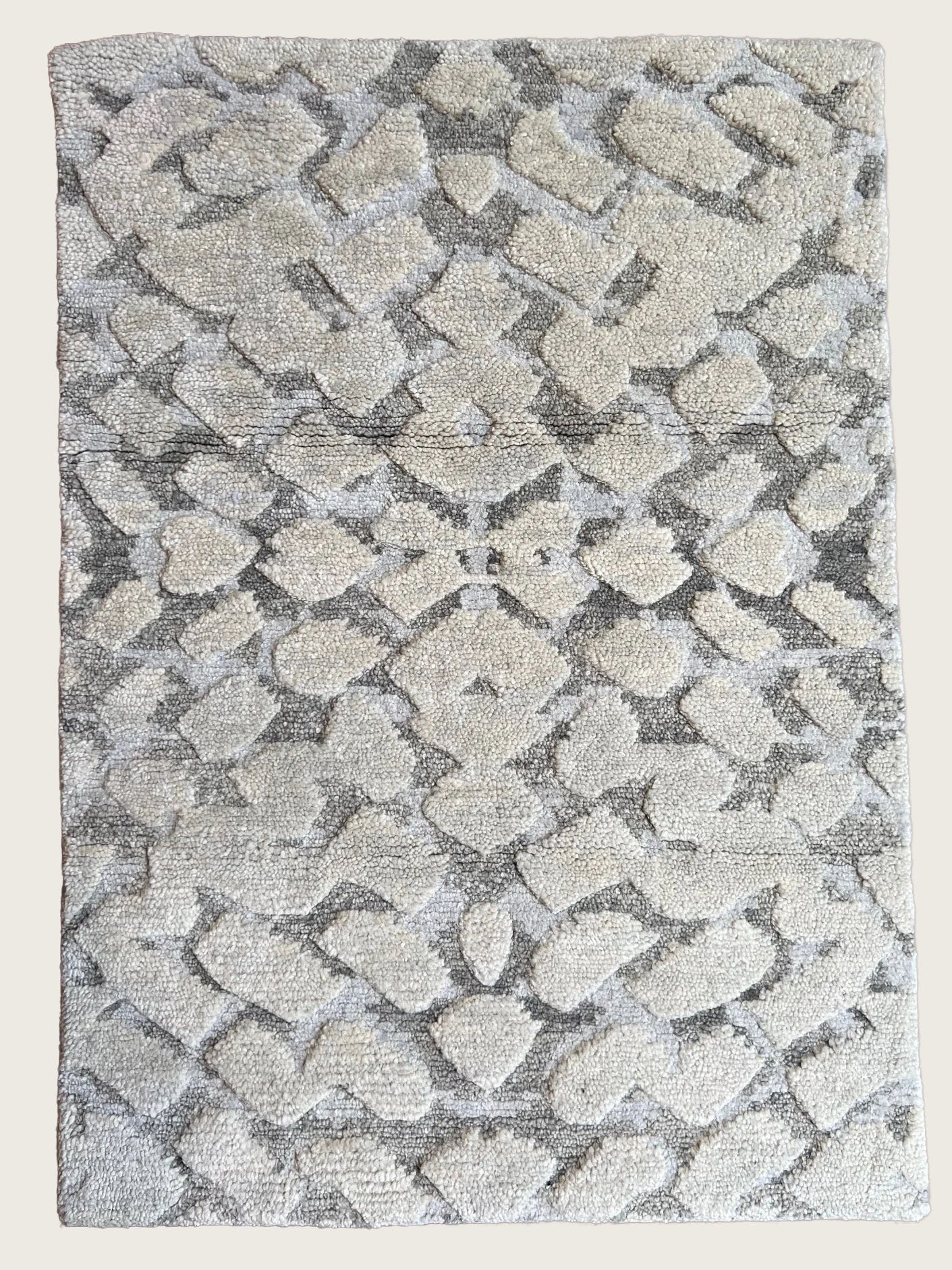 Close-up of a textured rug with a floral and geometric pattern in neutral beige and gray tones.