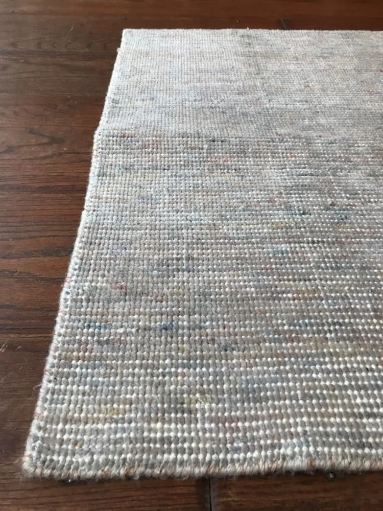 Close-up view of a beige, textured area rug on a wooden floor.