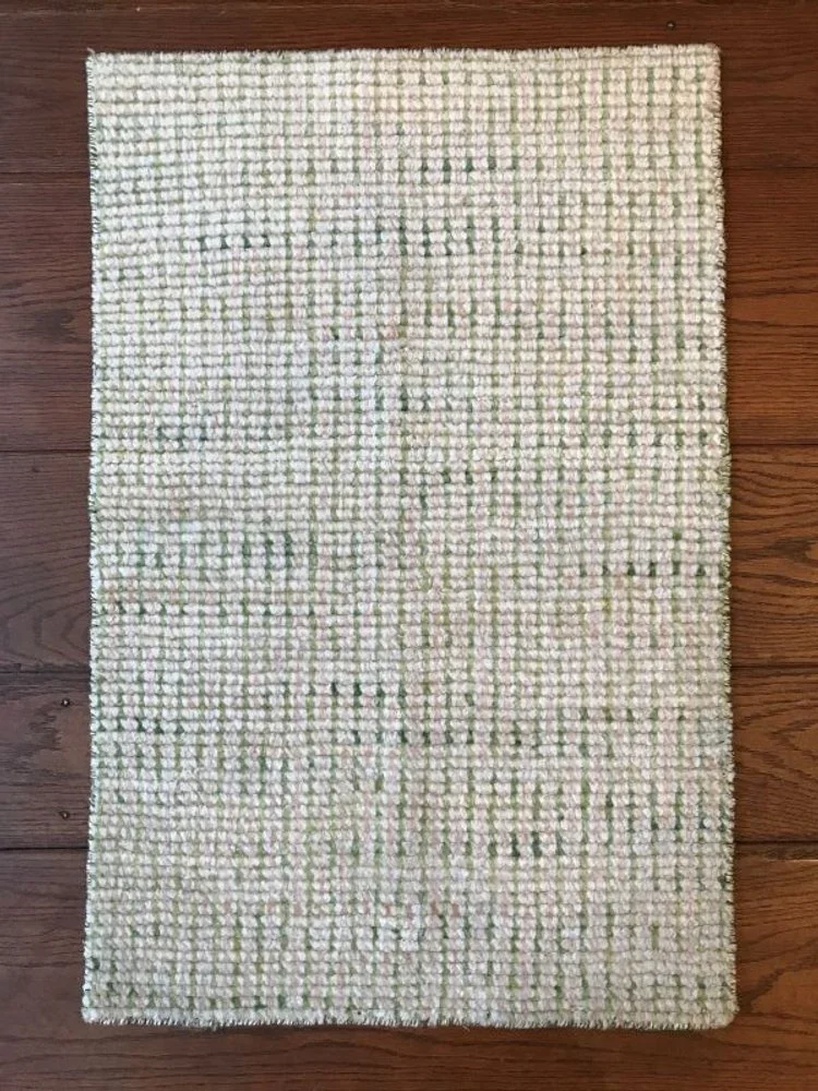 A rectangular area rug with a textured pattern in white and light green, placed on a wooden floor.