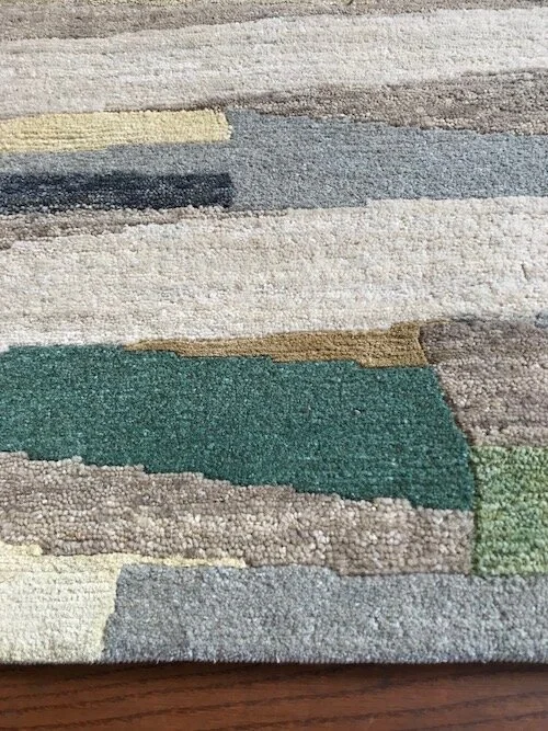Close-up of a multicolored abstract patterned rug with varying shades of green, beige, gray, and brown.