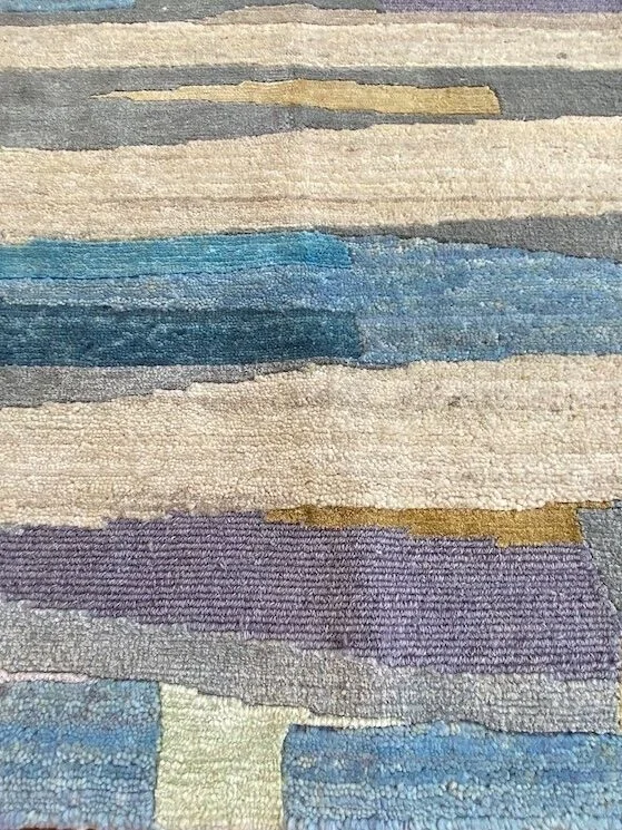 Close-up of a multicolored striped textured rug with shades of blue, purple, beige, and gold.