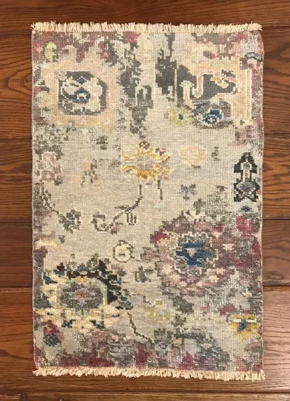 Small decorative area rug with floral and abstract motifs in muted tones of cream, gray, yellow, pink, and blue, placed on a wooden floor.