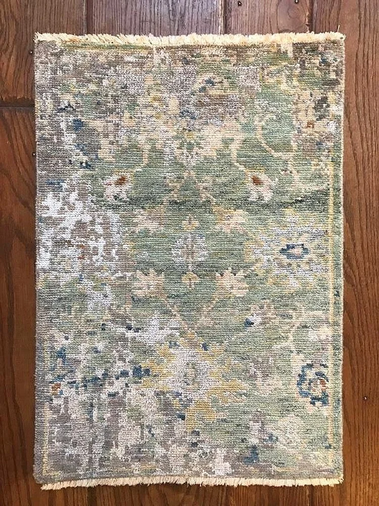 Small rectangular area rug with an intricate floral pattern in muted colors, placed on a wooden floor.