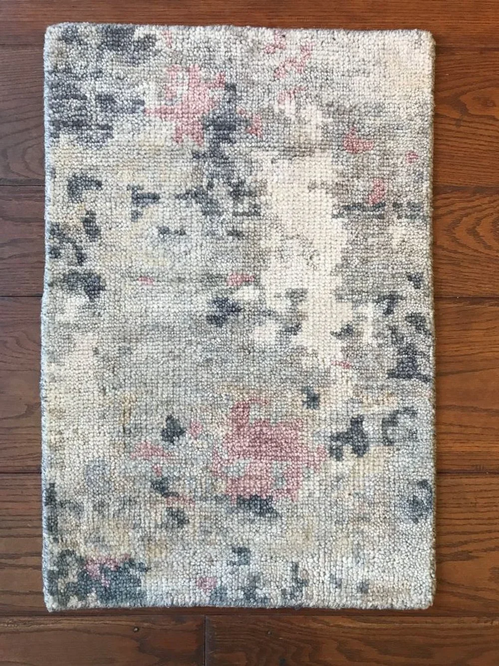 A rectangular area rug with a floral pattern in shades of beige, pink, and black on a wooden floor.