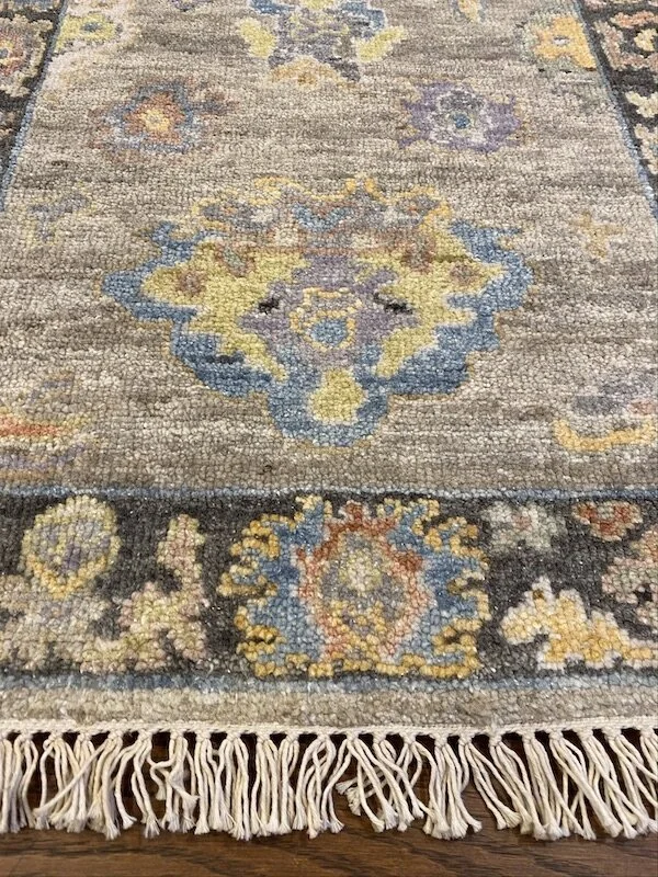 Close-up of a traditional patterned rug with floral and geometric motifs in shades of blue, yellow, beige, and black, and fringed edges.