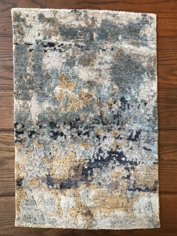 Rectangular abstract patterned area rug with beige, gray, black, and hints of blue and tan on a wooden floor.