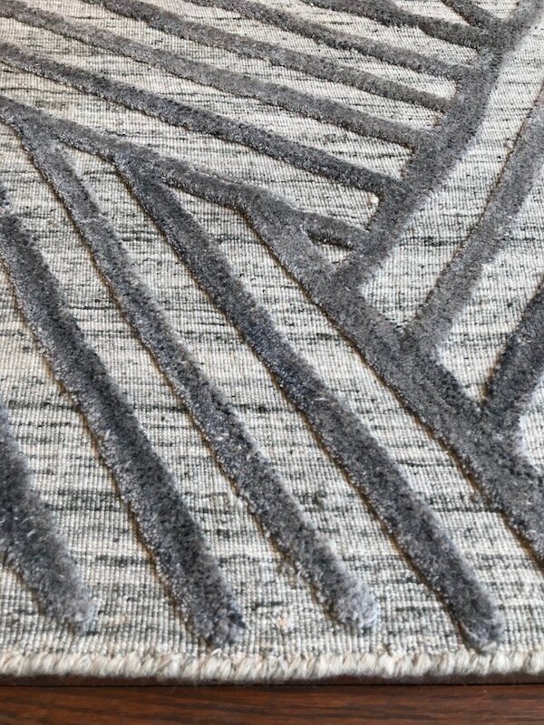 Close-up of a patterned rug with gray, black, and beige geometric lines on a hardwood floor