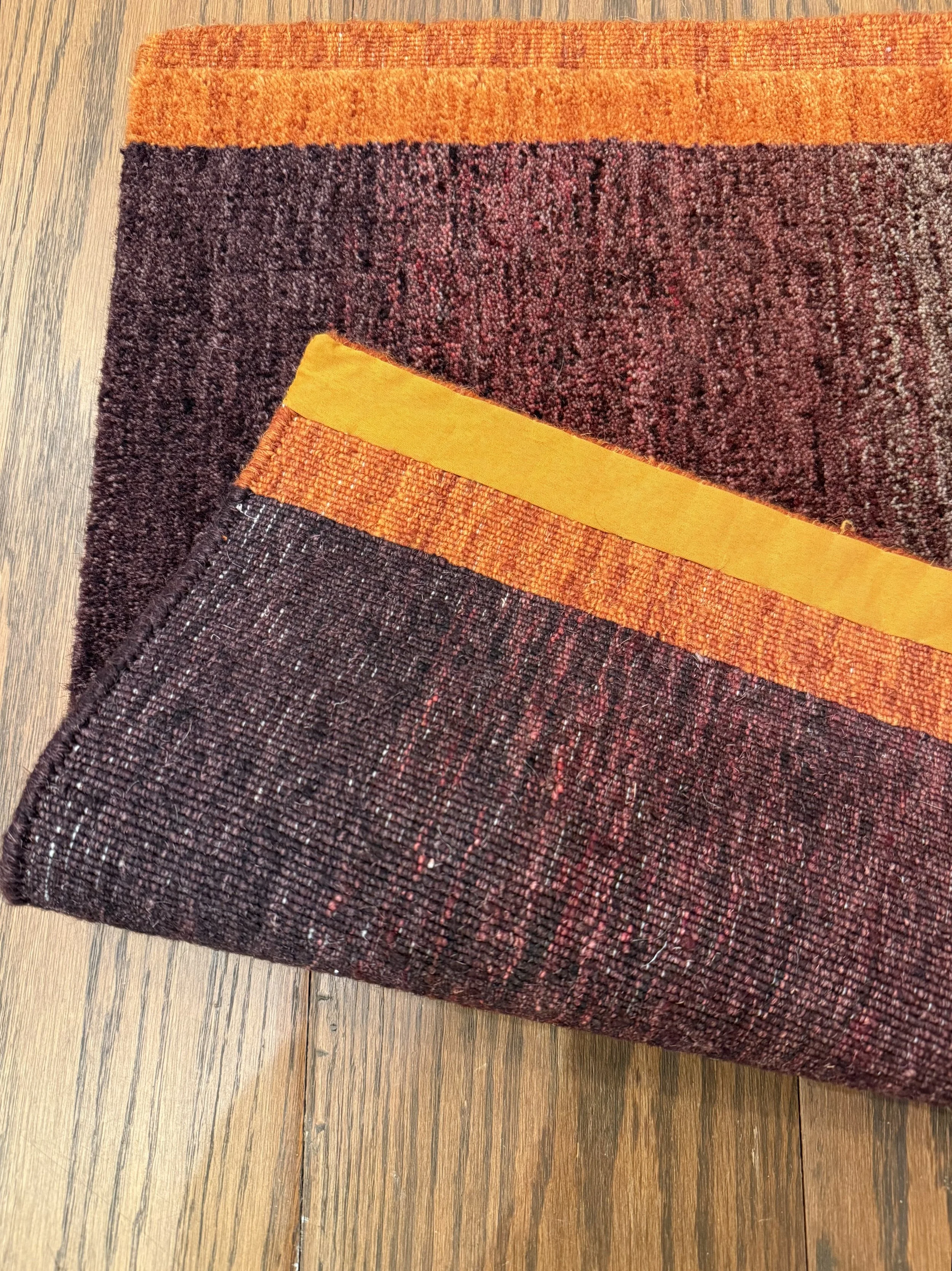 Close-up of a multicolored area rug with orange, yellow, black, and red sections, placed on a wooden floor.