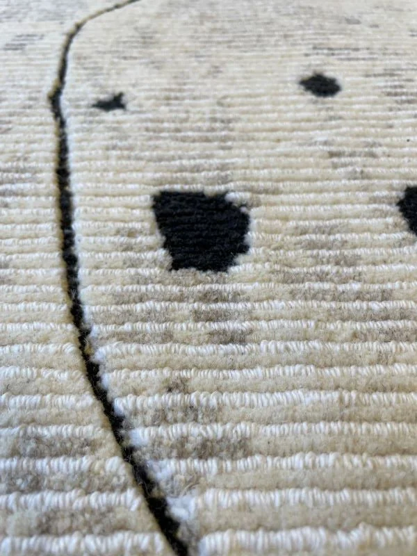Angled close-up image of a white rug with black dots and lines.