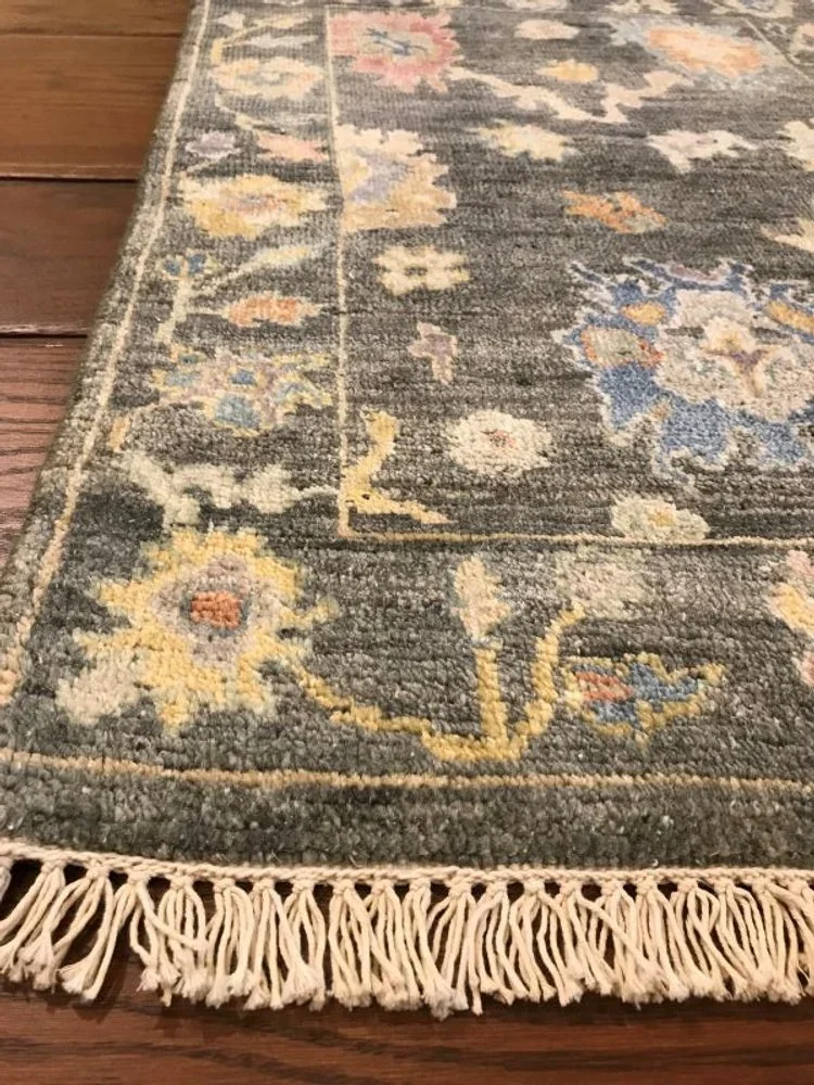 Close-up of a decorative area rug with floral patterns and fringed edges on a wooden floor.