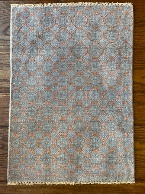 Light blue rug with a repeating geometric pattern of orange hexagons and diamonds, placed on a wooden floor.