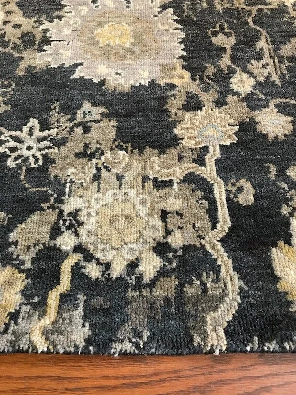 Close-up of a patterned area rug with floral and leaf designs in black, beige, and gray tones on a wooden floor.