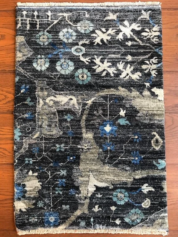 A rectangular area rug with a floral and abstract pattern in shades of navy blue, beige, light blue, and off-white on a wooden floor.