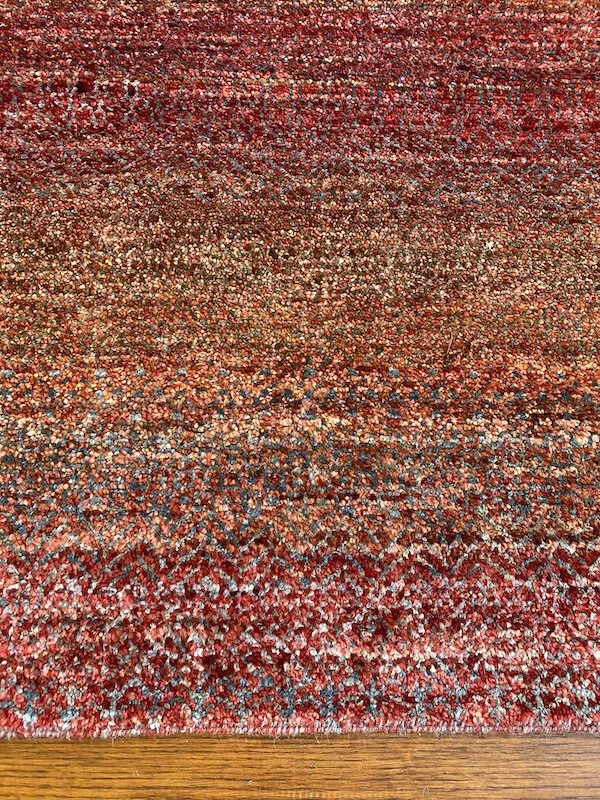 Close-up of a red, orange, and beige patterned area rug on a wooden floor.