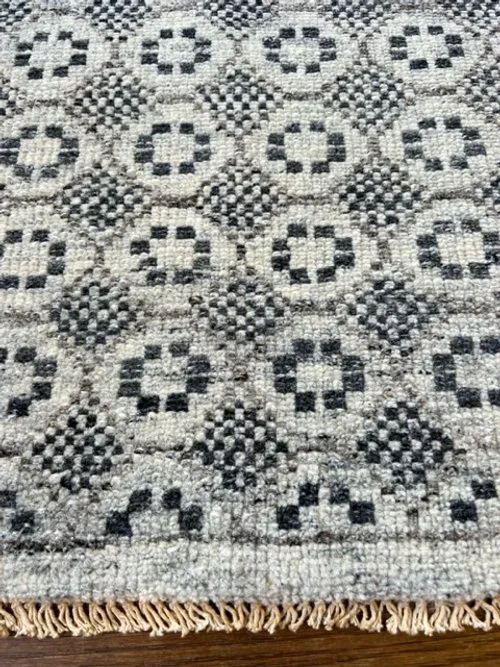 Close-up of a black and white patterned woven rug with fringe at the bottom.