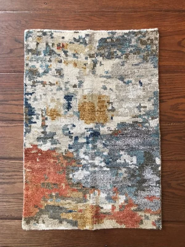 An abstract patterned area rug with blue, beige, rust, and cream colors on a hardwood floor.