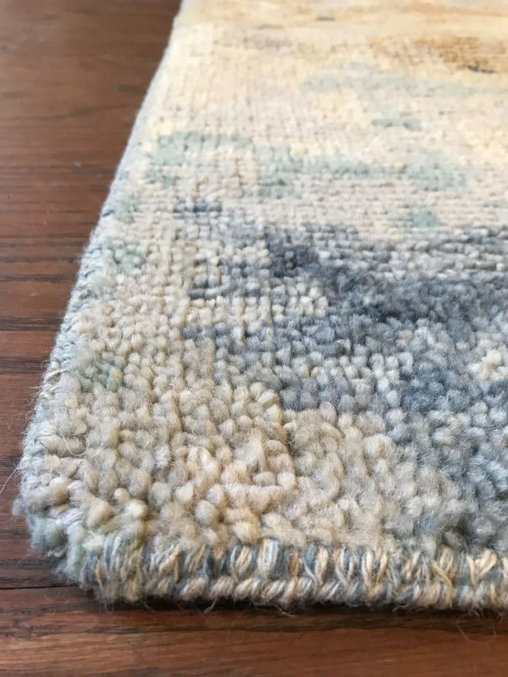 Close-up of a beige and gray patterned rug on a wooden floor, showing some dirt and debris.