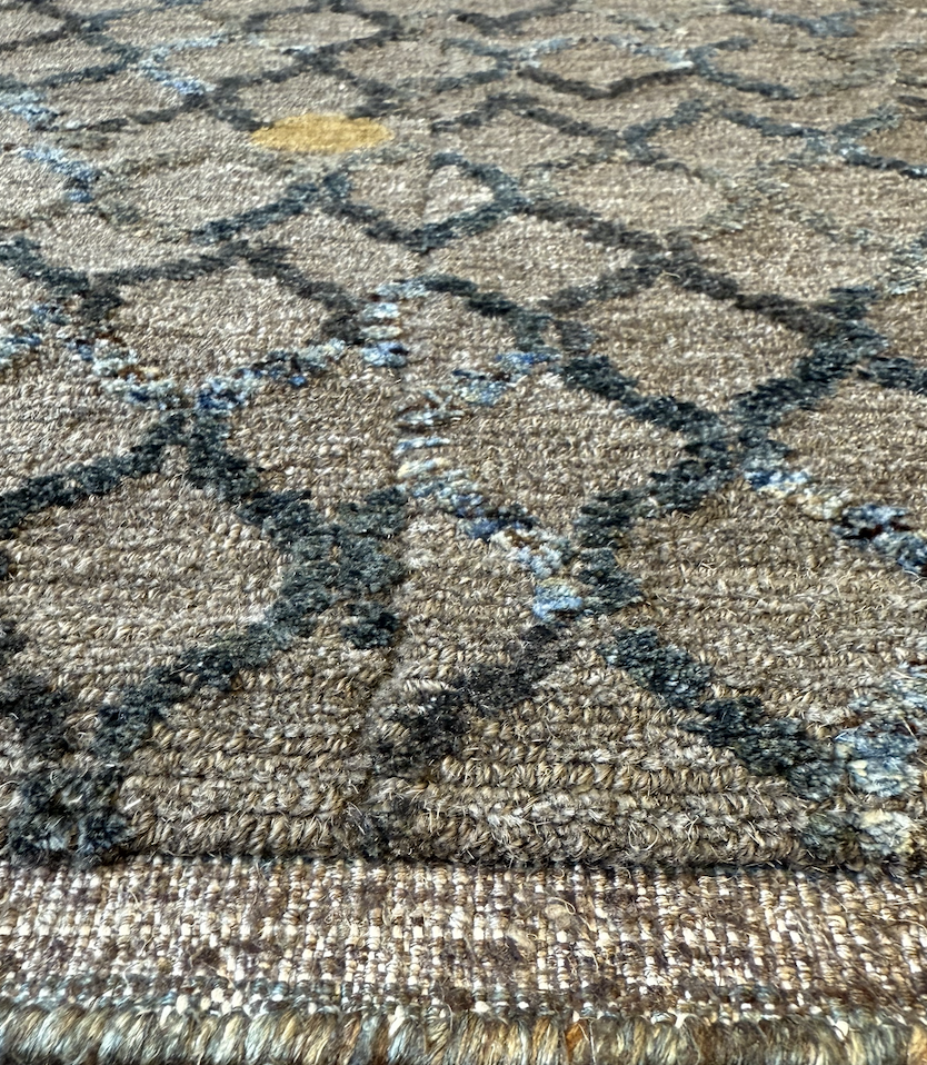 Close-up of a patterned carpet with a diamond design in black and blue on a tan background.