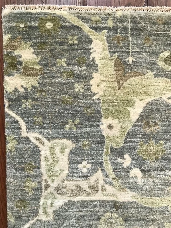 Close-up of a decorative area rug with a floral and leaf pattern in shades of green, cream, and gray on a hardwood floor.
