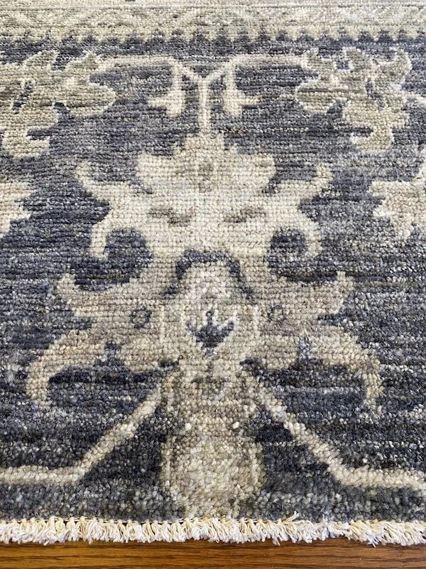 Close-up of a detailed patterned area rug with floral and geometric designs in beige, gray, and dark blue tones.