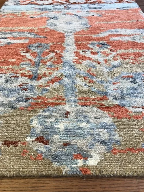 Close-up of a decorative area rug with a floral pattern featuring blue, beige, and orange colors.