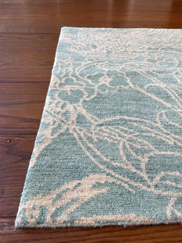 A close-up of a light blue and beige patterned area rug on a wooden floor.