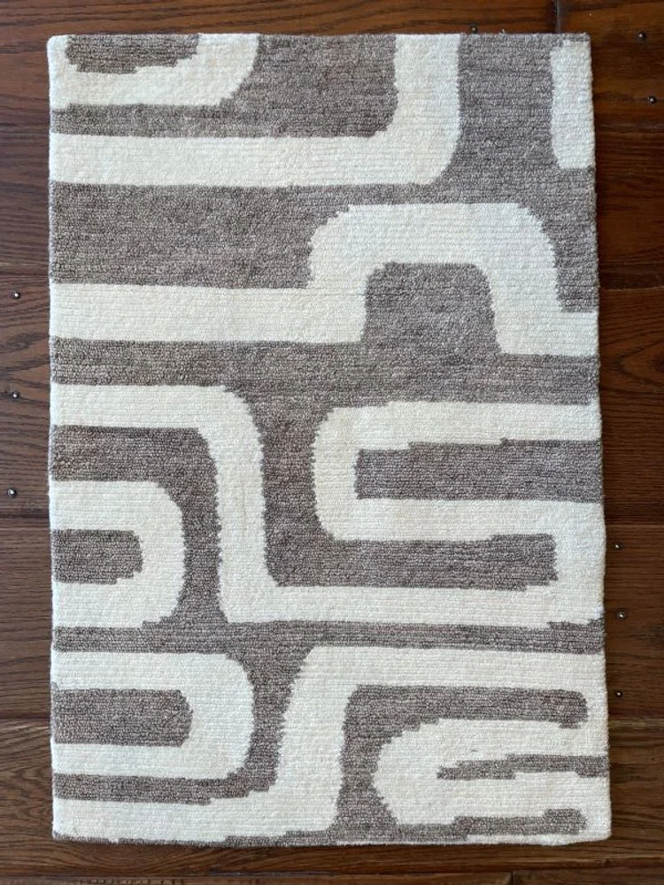 A rectangular area rug with a geometric maze pattern in beige and brown on a wooden floor.