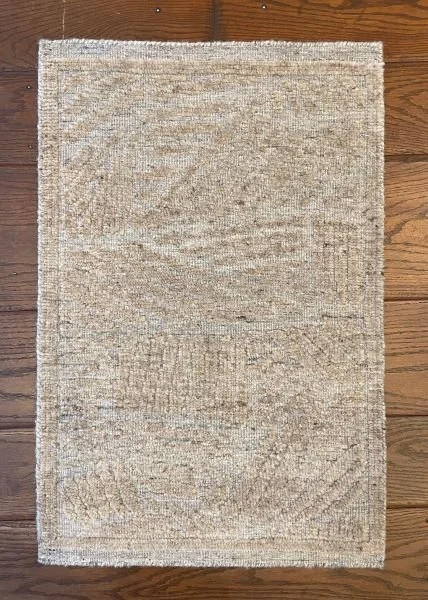 A beige rectangular area rug with a subtle pattern on a wooden floor.