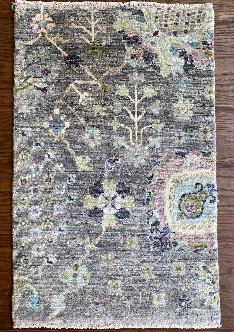 A patterned area rug with floral and geometric designs in muted pastel colors on a wooden floor.