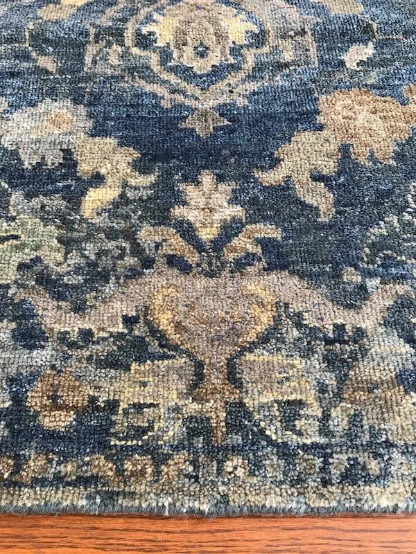 Close-up of a vintage patterned area rug with floral and geometric designs in beige and dark blue colors on a wooden floor.