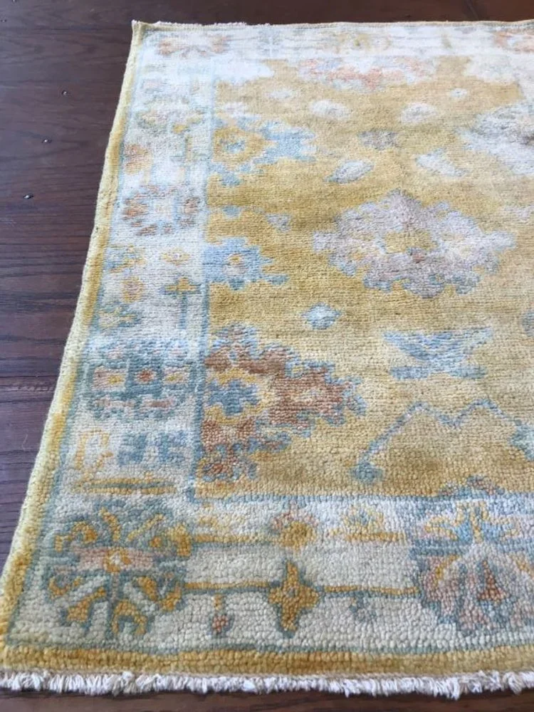 A traditional area rug with a floral pattern in pastel colors, placed on a wooden floor.