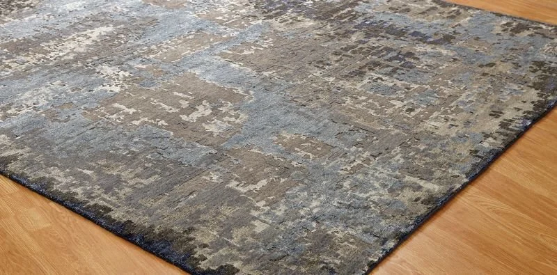 Close-up of an area rug with a distressed pattern in shades of blue, gray, and beige on a wooden floor.