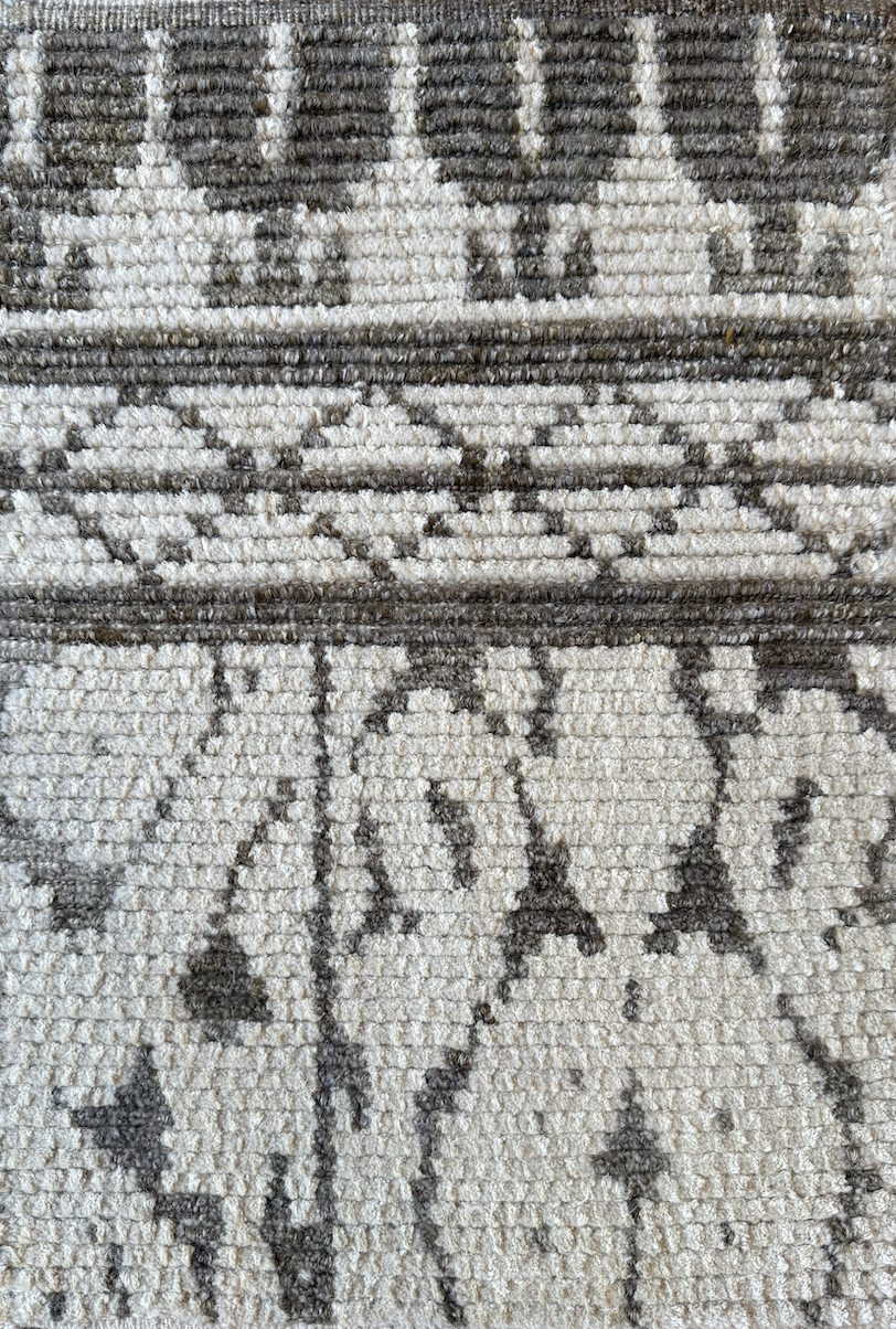 Close-up of a woven rug with a floral and geometric design in beige and dark gray colors.