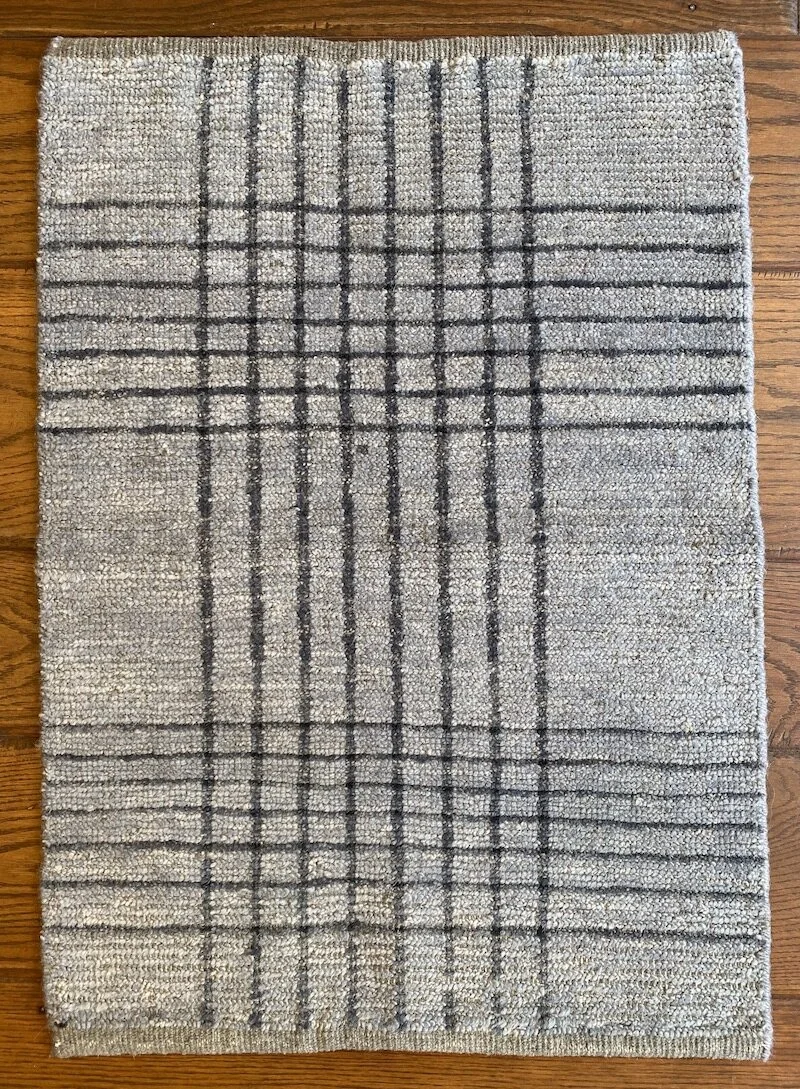 Gray and beige patterned area rug with black grid lines, placed on hardwood floor.
