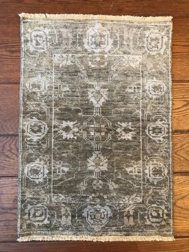 A vintage-style rectangular area rug with a distressed pattern in shades of gray and beige, placed on a wooden floor.