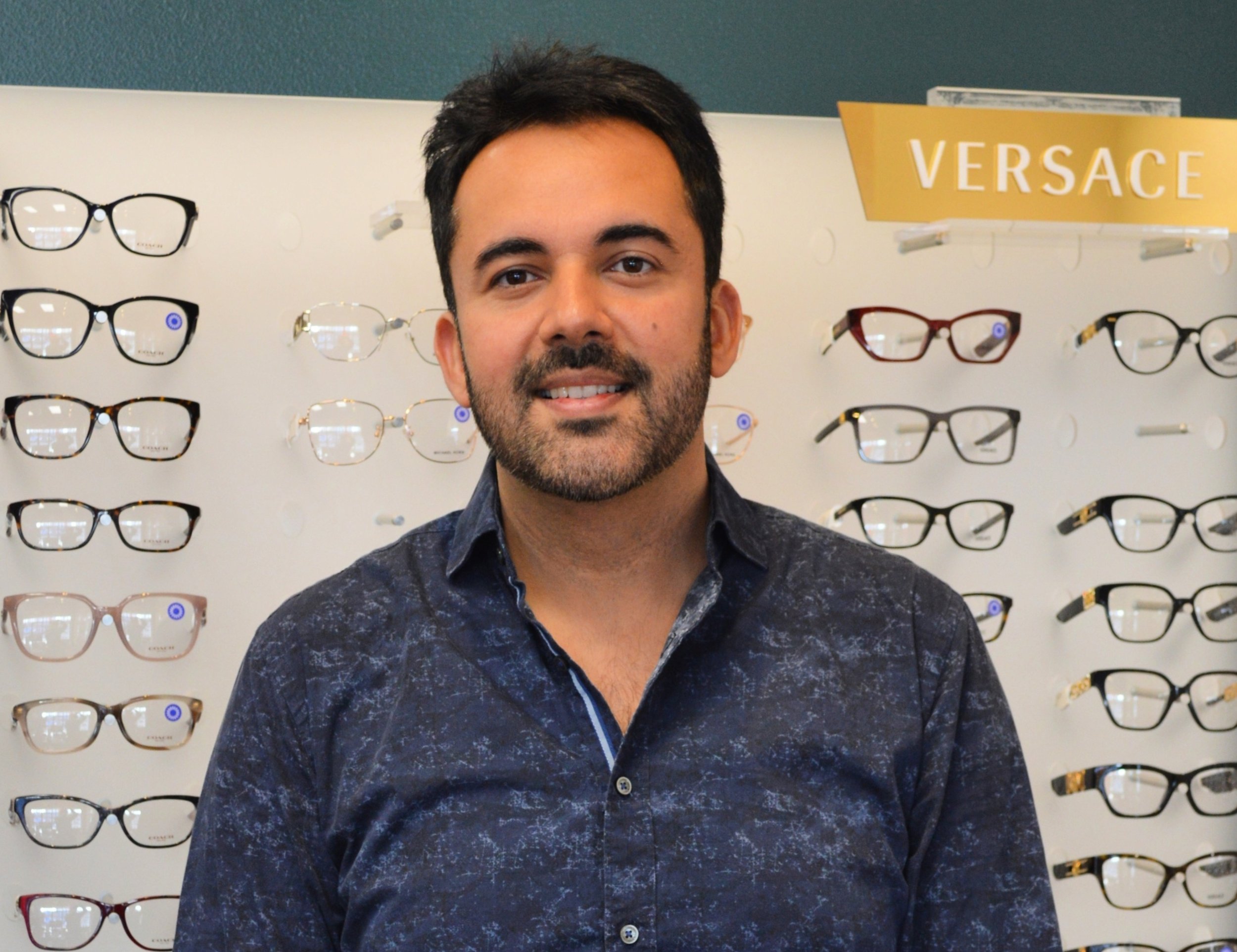 Dr. Rohit Sachdeva standing in front of a Versace Frame board at ClearView Eyecare