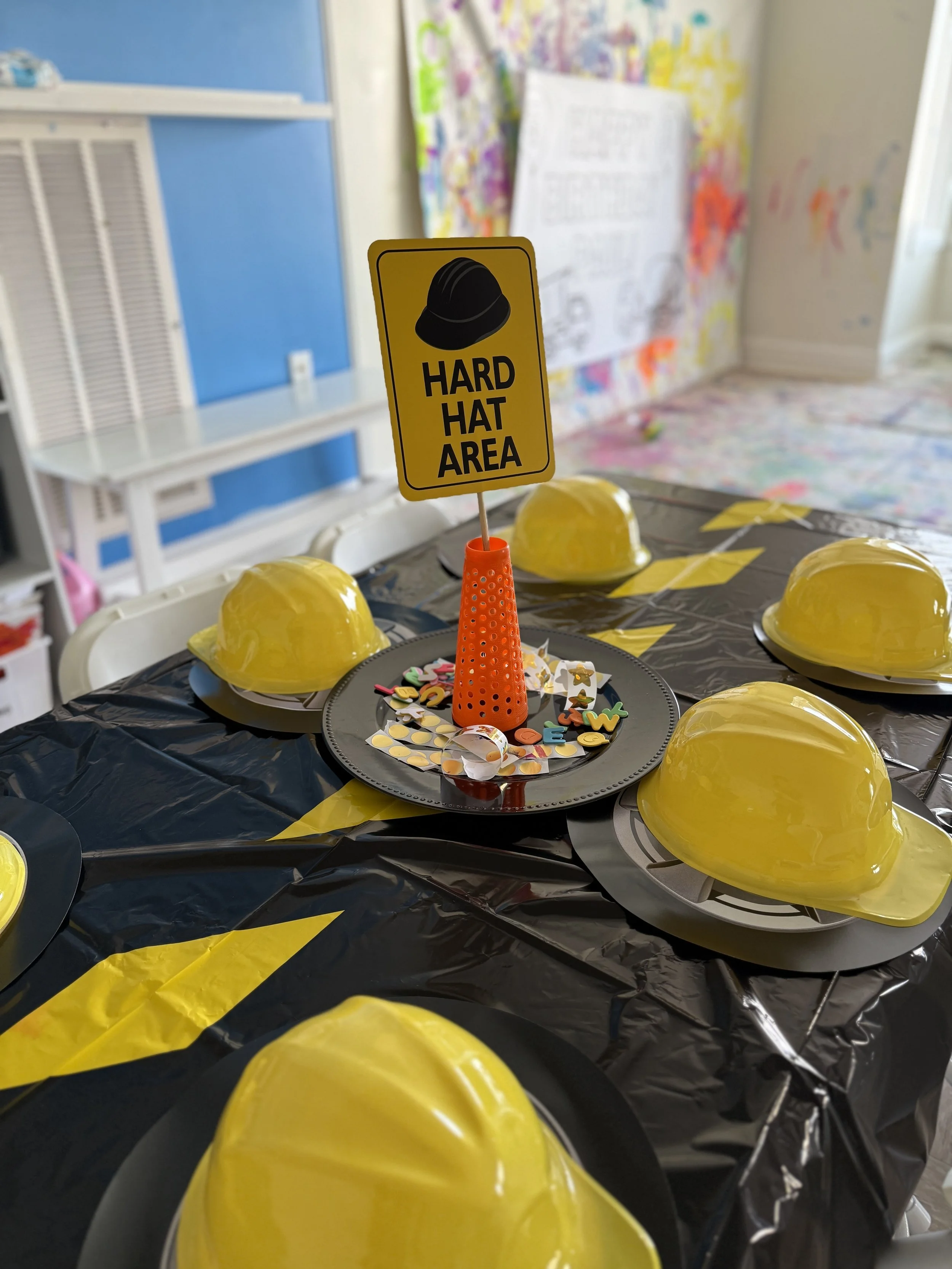 Party table decorated with yellow construction helmets as helmets, a sign that reads "Hard Hat Area" with a construction hat icon, and confetti.